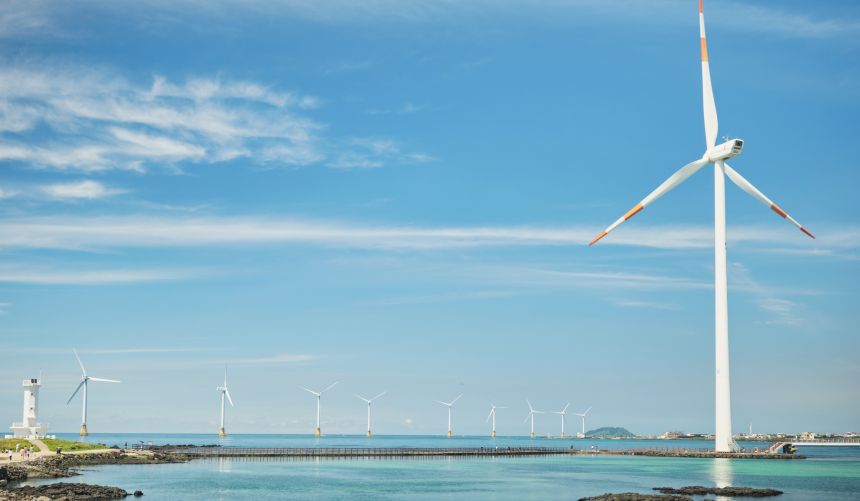 Ten windmills by the ocean with blue sky.