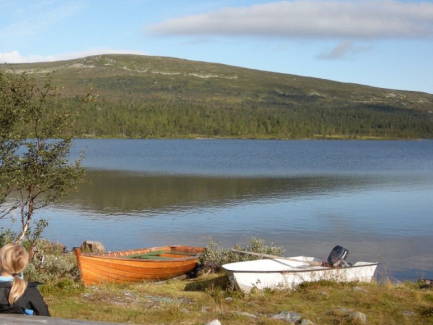 Person ser utover stille innsjø og to småbåter på land. 