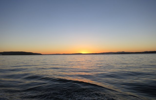 Bilde av stille vann i solnedgang.