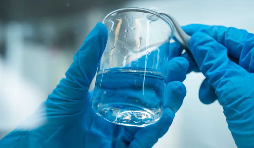 Hands in blue gloves holding glass container with liquid
