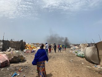 Besøk på uformelle gjenvinningssteder, India. (Foto: Emmy Nøklebye, NIVA) En gruppe mennesker på et sted med mye avfall, røyk i bakgrunnen.