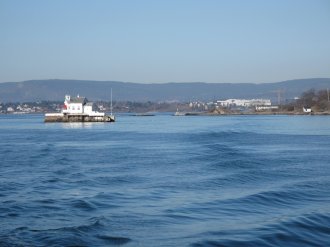 Bygning på liten holme i stille fjord. 